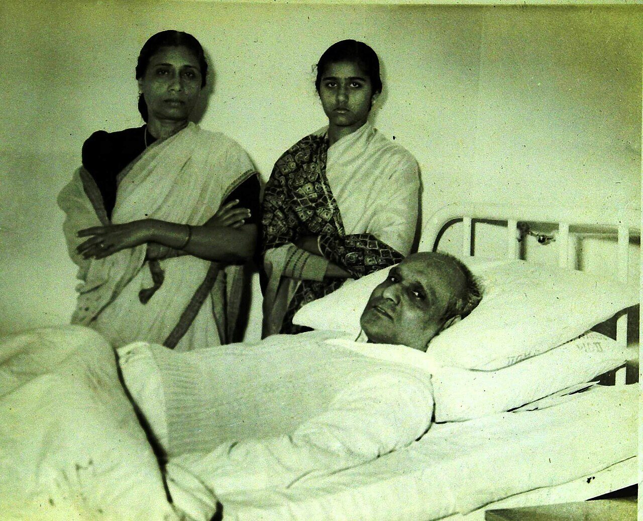 Batukeshwar Dutt lying in a hospital bed during his final illness, with his wife Anjali and daughter Bharati standing behind the bed.